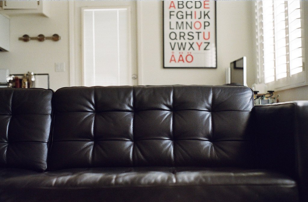 A living room photo with a black leather sofa and an alphabet poster on the wall
